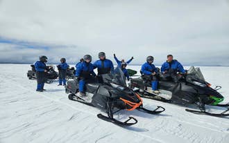 A group in blue suits prepares for a Langjokull Glacier snowmobile tour under bright midday skies.