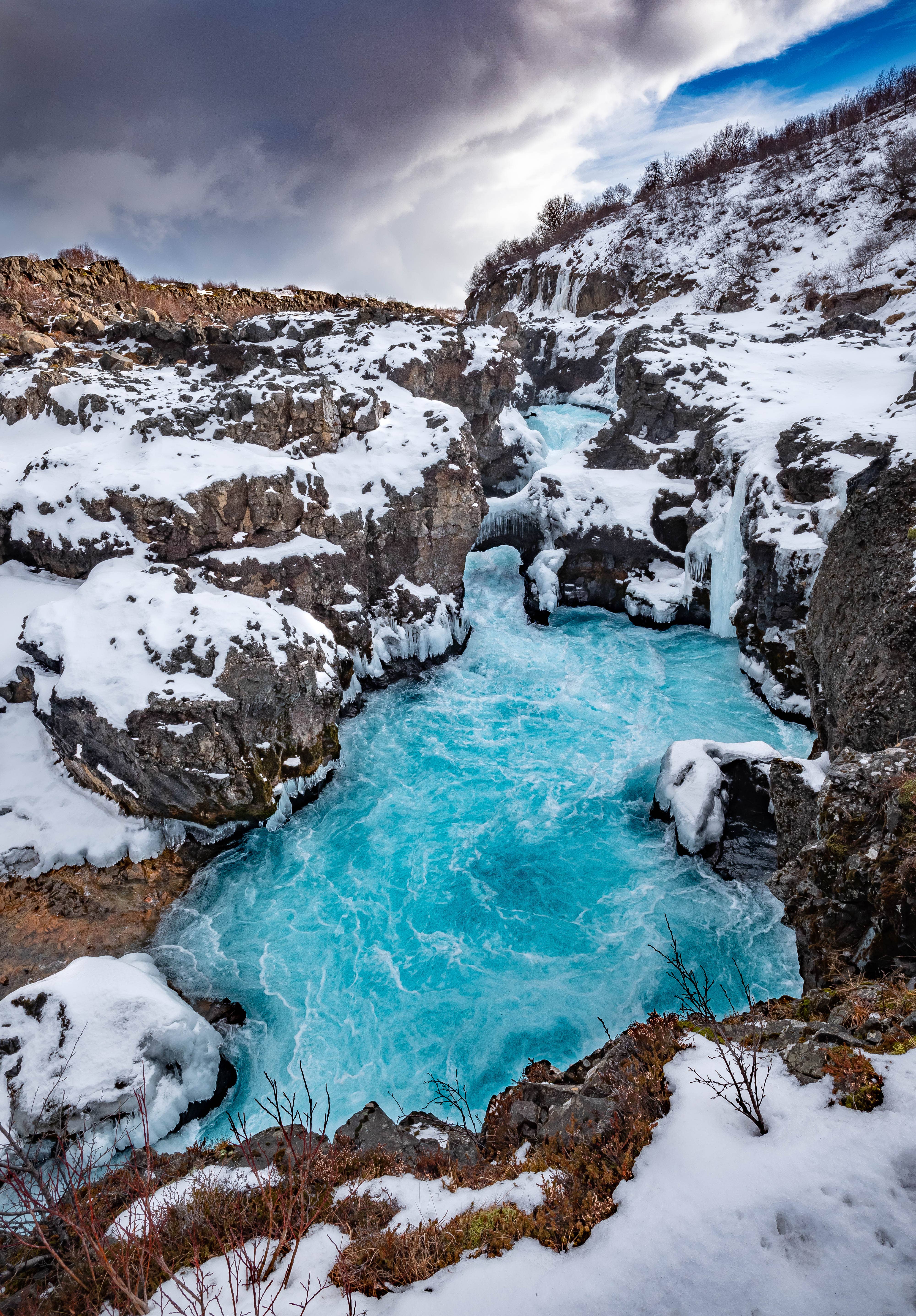 Barnafossar Waterfalls in West Iceland, with bright blue glacial water rushing through a narrow rocky channel.