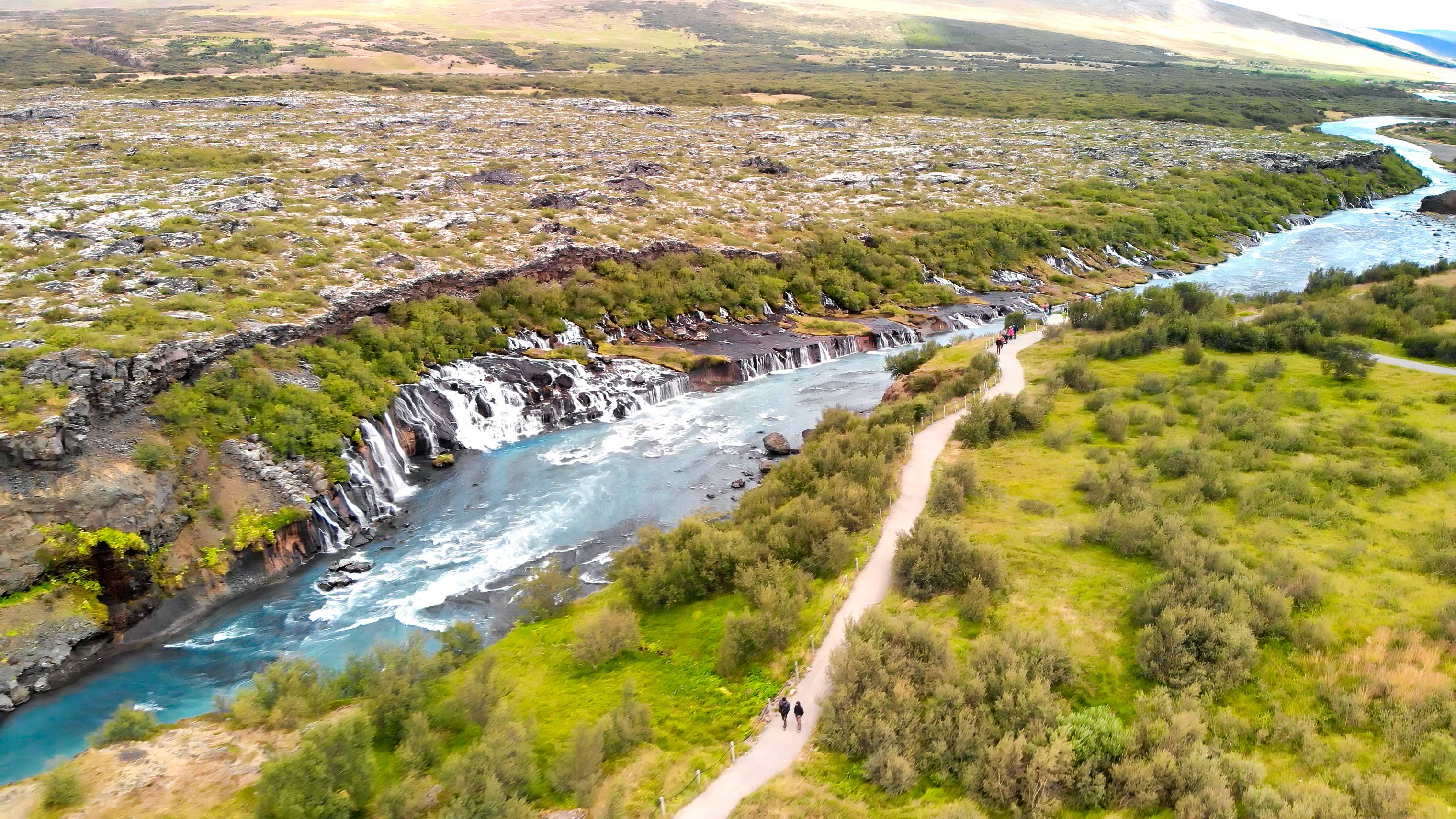 Hraunfossar Waterfalls in West Iceland, with streams of clear water flowing from lava fields into a blue river.