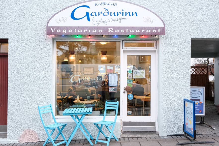 雷克雅未克Kaffihusid Gardurinn入口，蓝色外墙，设有户外座位和素食标识。