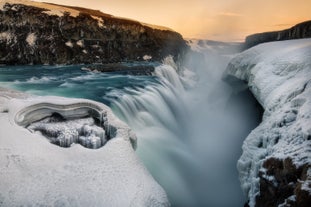 Gullfoss Waterfall appears partially frozen in winter, surrounded by ice and snow.