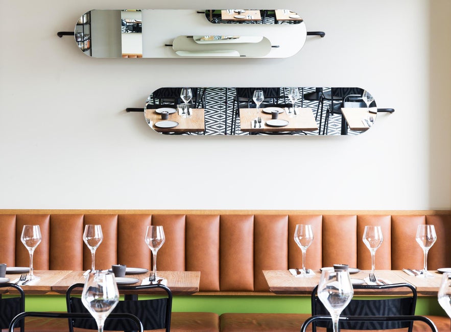 Seating at MatBar in Reykjavik with leather bench, wooden tables, wine glasses, and wall mirrors.