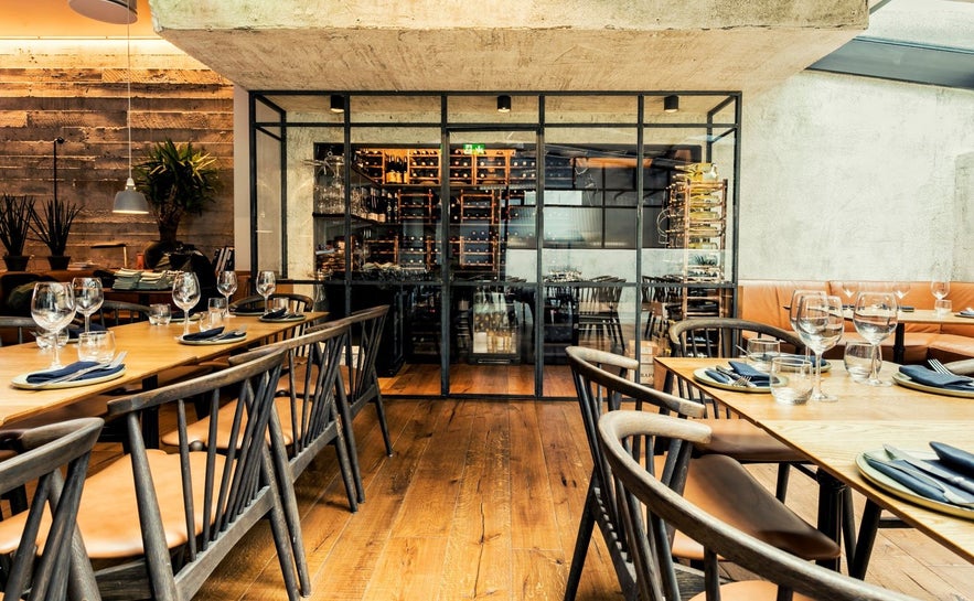Dining area of Sumac in Reykjavik with rustic walls, wood tables, and wine glasses.