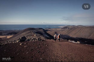 People walk along stark and hilly volcanic terrain on the Reykjanes Peninsula with the sea beyond.