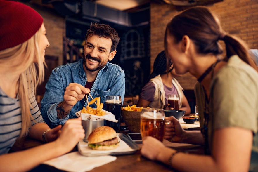 Friends enjoying burgers, fries, and beer together at a lively food hall on the South Coast of Iceland
