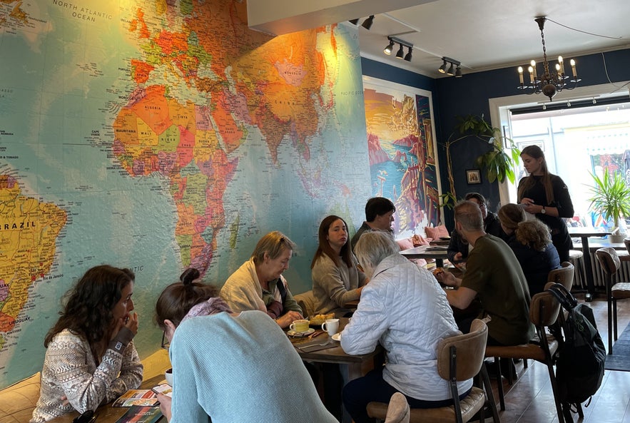 Interior of Salka Valka in Reykjavik with world map mural, wooden furniture, diners, and natural lighting.
