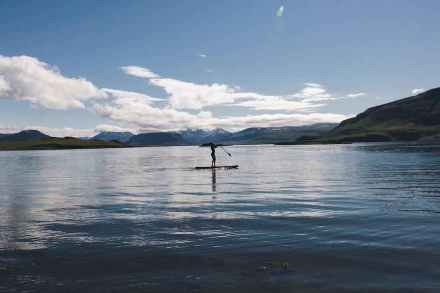 Person paddle boarding at Hvammsvik Hot Springs with beautiful Hvalfjodrur in the background