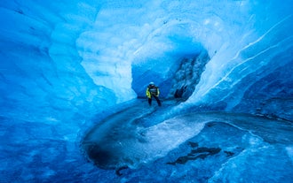 A person explores a shimmering blue ice cave in Iceland, surrounded by smooth, translucent walls formed by centuries of glacial ice.
