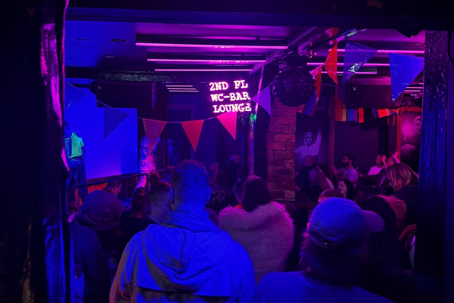 Interieur van Kiki Queer Bar in Reykjavik met regenboogversiering en een liveoptreden van een dragartiest op het podium.
