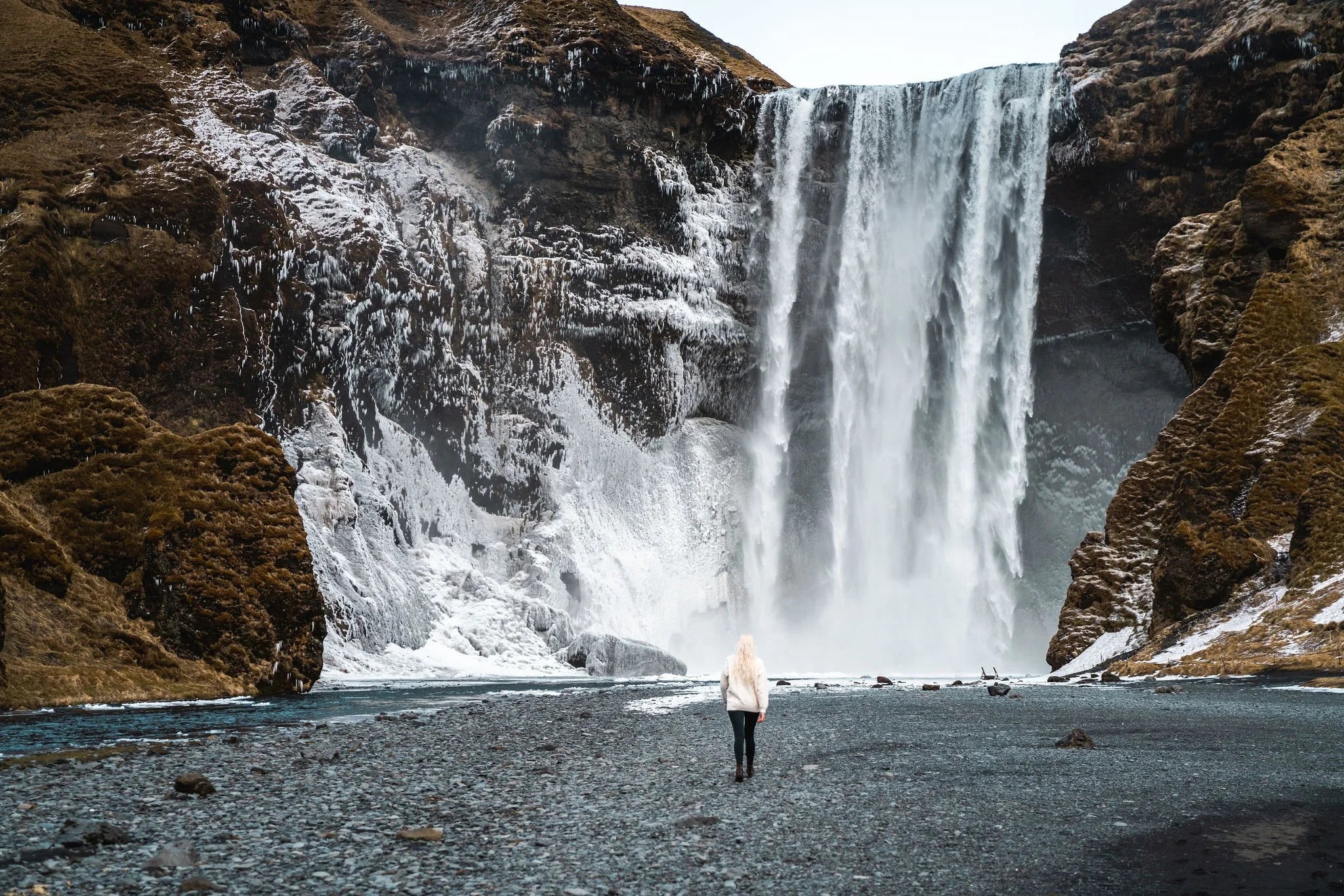 A traveler walks toward Skogafoss Waterfall cascading down icy cliffs on Iceland’s South Coast.