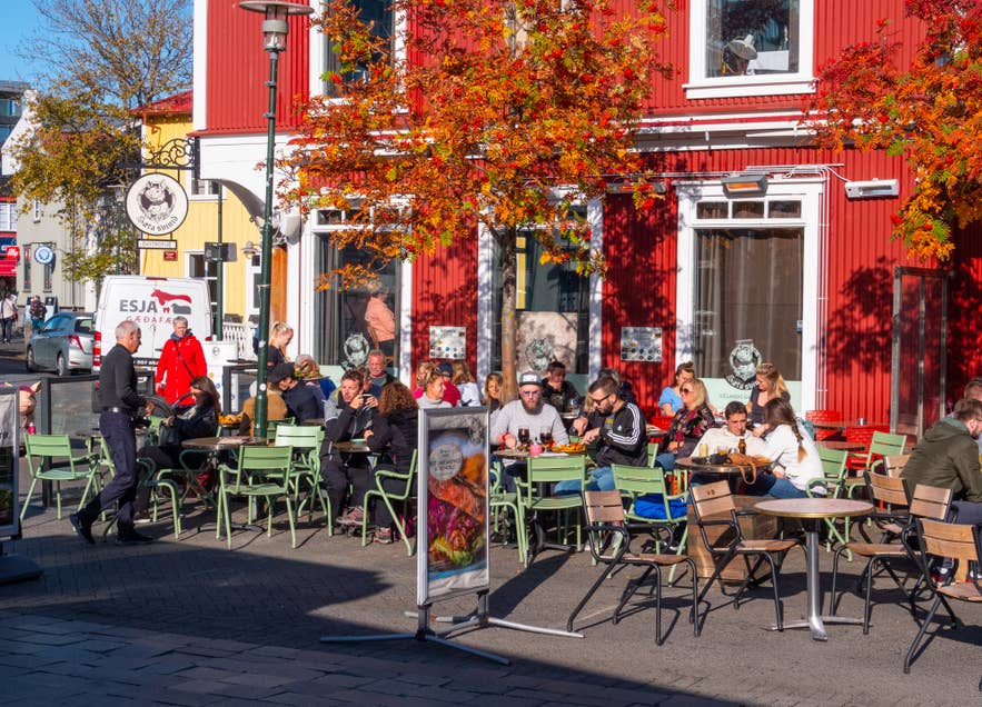 Sæta Svínið in downtown Reykjavik with people dining on a sunny autumn day beside colorful Icelandic buildings.