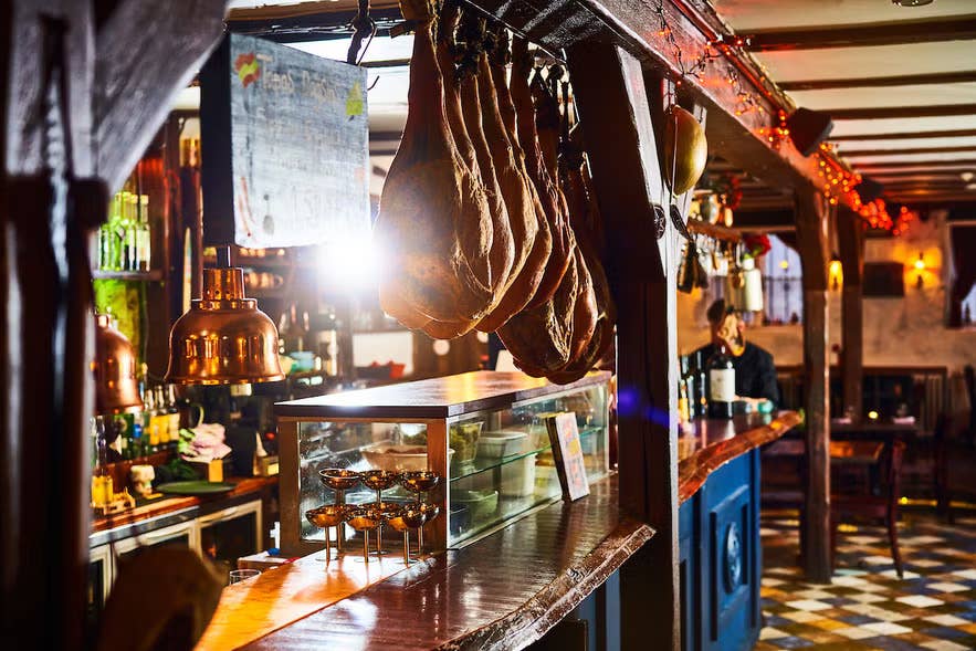 Rustic interior of Tapas Barinn in Reykjavik with hanging cured meats, warm lighting and traditional wooden bar.