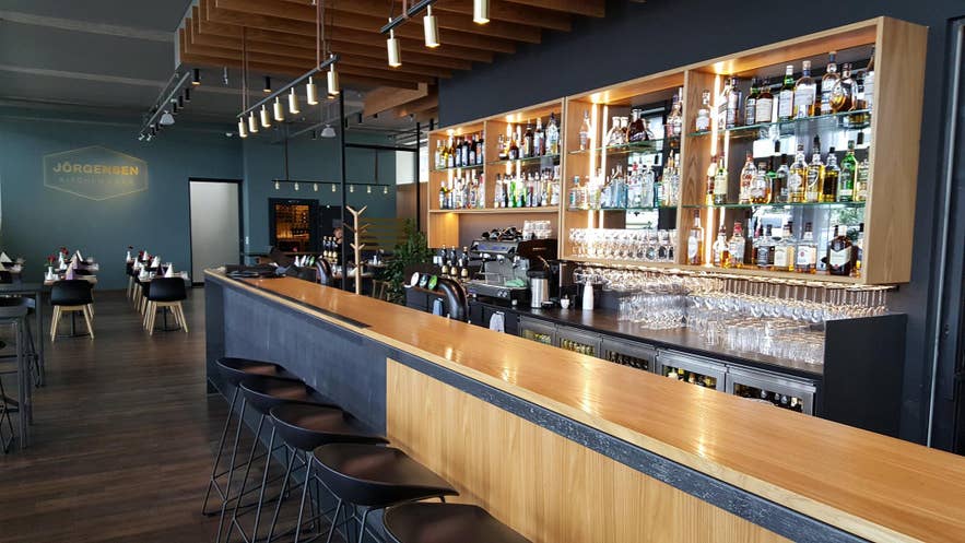 雷克雅未克 Jörgensen Kitchen & Bar 的现代鸡尾酒吧内部装潢时尚，配有木质吧台、酒类展示架和时尚座椅。