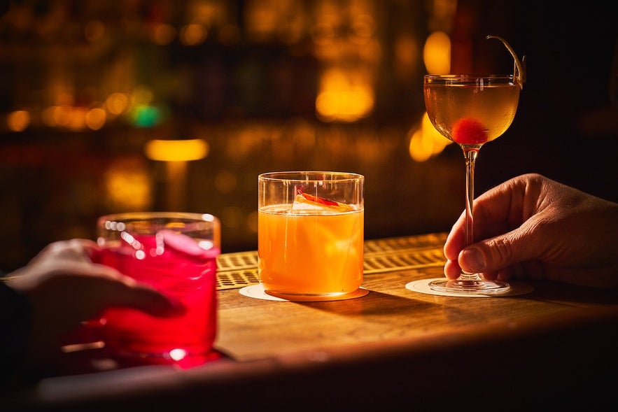 Three cocktails at Tipsy Bar & Lounge in Reykjavík, Iceland on a dimly lit counter with warm lighting and cozy atmosphere. Three cocktails at Tipsy Bar & Lounge in Reykjavík, Iceland on a dimly lit counter with warm lighting and cozy atmosphere.