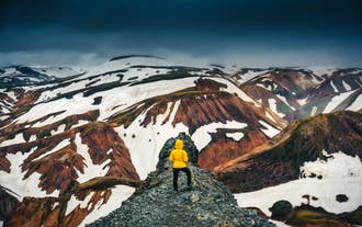 Person in yellow jacket standing on a ridge overlooking colorful rhyolite mountains in Landmannalaugar, Iceland