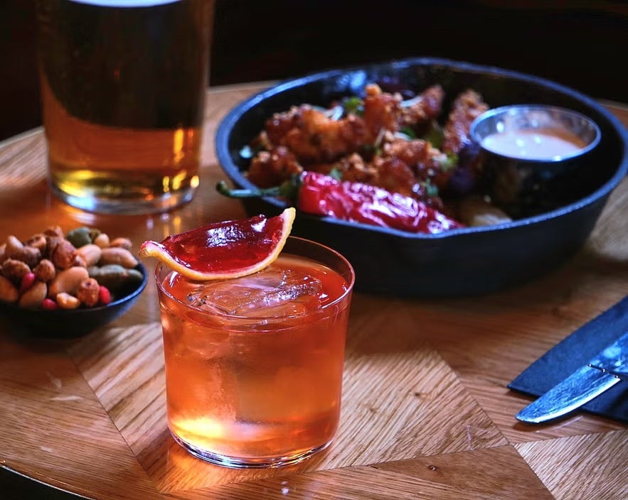 A signature cocktail garnished with a dried orange slice on a wooden table at Tipsy Bar & Lounge in Reykjavik.