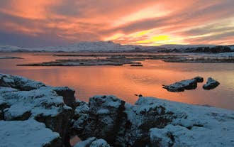 Schneebedeckte Spalte und See im Þingvellir-Nationalpark bei einem lebhaften Wintersonnenuntergang.
