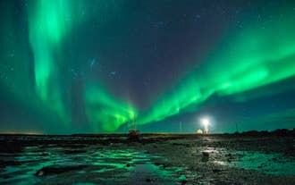Aurores boréales vert vif au-dessus d'un phare et de la côte lors d'une excursion en Super Jeep au départ de Reykjavik.