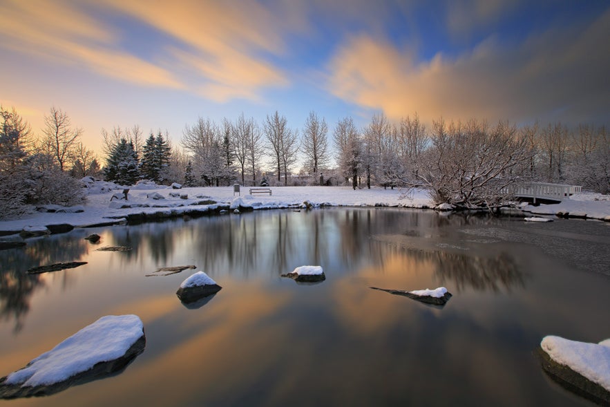 Tjornin Pond in Reykjavik frozen and covered in snow, with the soft sunset light adding charm to the winter scene.