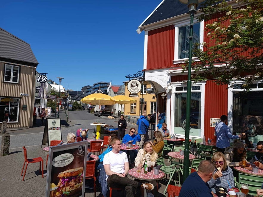 People enjoy food and drinks at outdoor tables under yellow umbrellas at Sæta Svínið Gastropub in downtown Reykjavik.