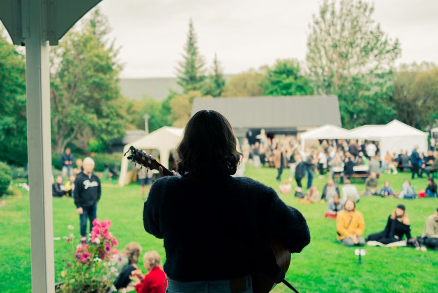 Musician performs for a seated crowd during an outdoor concert at Akureyri Botanical Gardens.