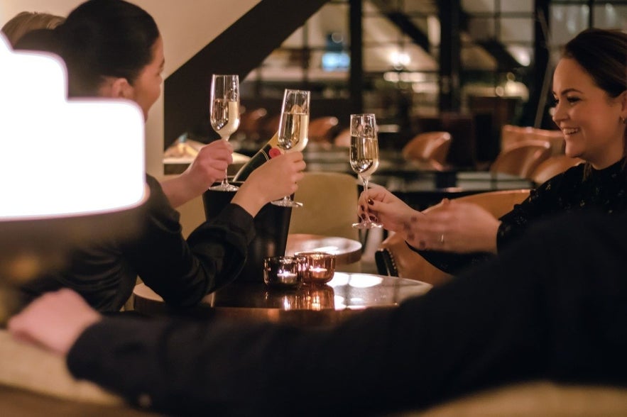 Friends toast with champagne glasses in Risið Vínbar, enjoying an evening of conversation and celebration.