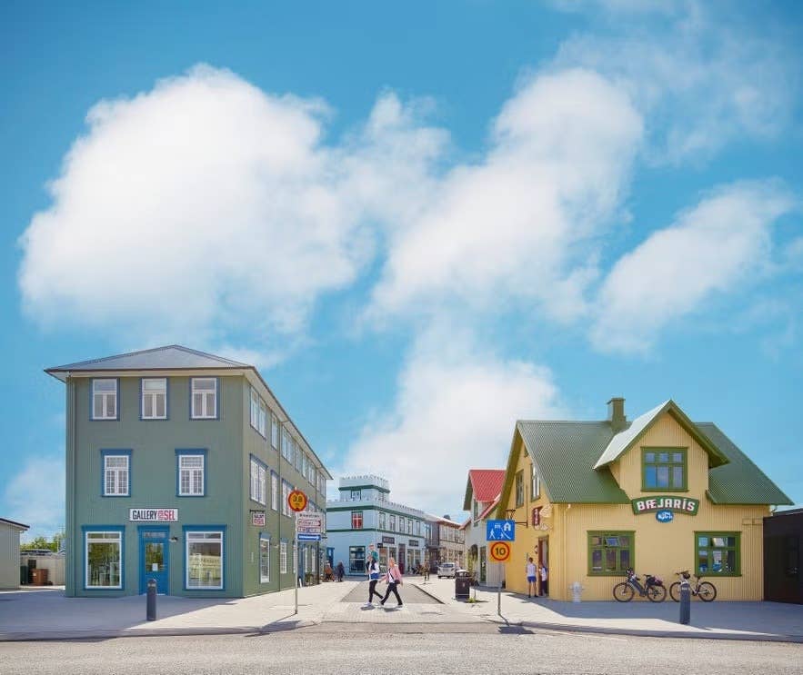 People stroll through the New Old Town in Selfoss, Iceland, surrounded by colorful historic-style buildings under a bright blue sky.