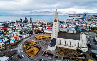 Aerial view of Hallgrimskirkja Church towering over Reykjavik with mountains and sea beyond.