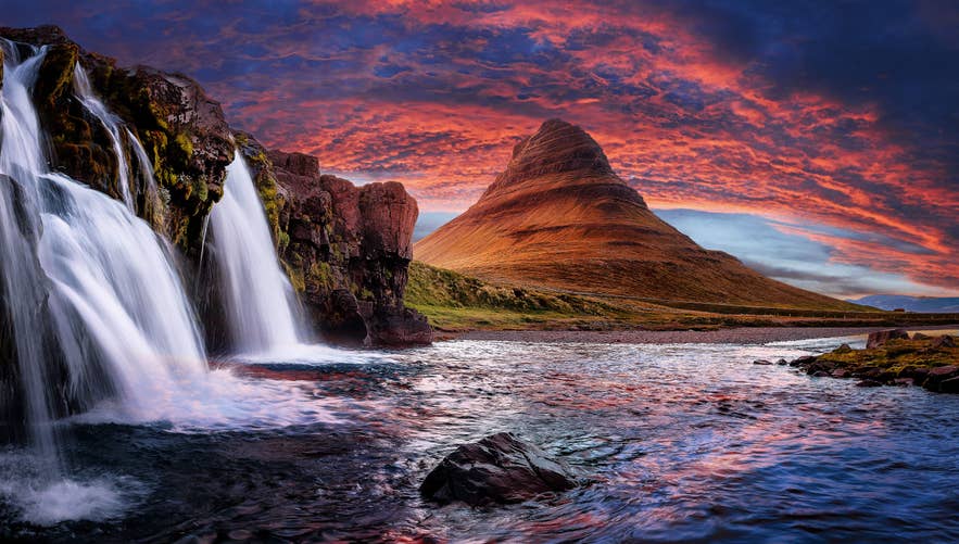 Der Berg Kirkjufell und der Wasserfall Kirkjufellsfoss unter einem leuchtend roten und violetten Sonnenuntergang auf der Halbinsel Snaefellsnes in Westisland.
