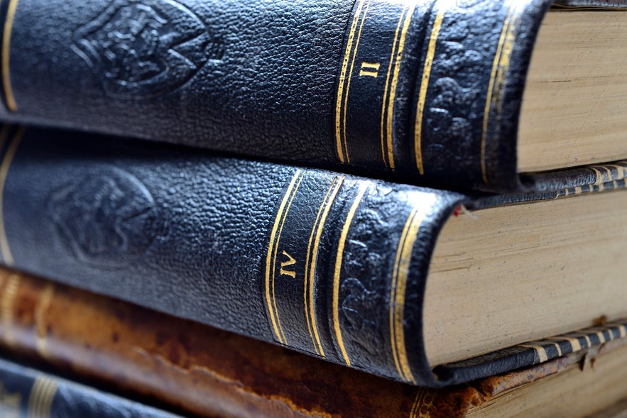 Close-up of stacked Icelandic saga books with black leather covers, gold embossed details, and visible Roman numerals on the spines.