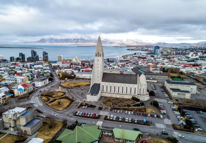 Aerial view of Hallgrimskirkja church and downtown Reykjavik with colorful buildings and mountains across the bay.