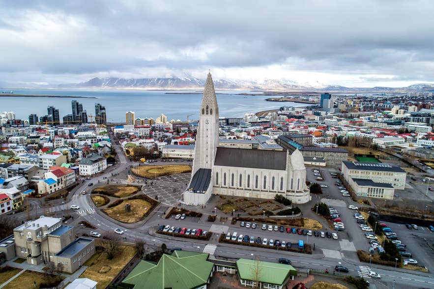 Aerial view of Hallgrimskirkja church and downtown Reykjavik with colorful buildings and mountains across the bay.