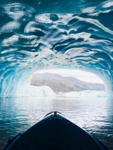 Kayaking inside a blue ice cave in Iceland with glacier lagoon views and rugged mountain landscape beyond.