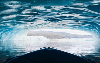 Kayaking inside a blue ice cave in Iceland with glacier lagoon views and rugged mountain landscape beyond.