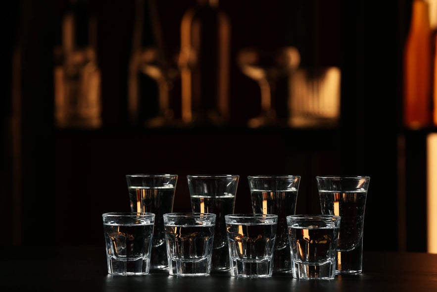 Shot glasses filled with clear brennivin in Iceland, arranged on a bar counter under warm ambient lighting Shot glasses filled with clear brennivin in Iceland, arranged on a bar counter under warm ambient lighting