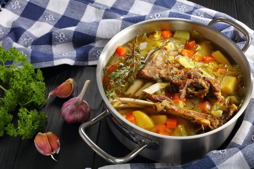 Kjotsupa lamb soup in a pot with potatoes, carrots, and herbs on a table, a classic Icelandic delicacy