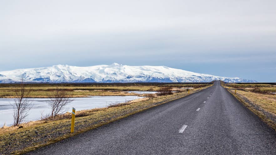 Eine lange Straße, die zum schneebedeckten Gletscher und Vulkan Eyjafjallajökull im Süden Islands führt.