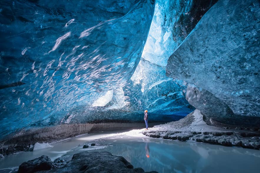 Viaggiatore all’interno di una grotta di ghiaccio blu nel ghiacciaio Vatnajokull, Islanda, circondato da pareti di ghiaccio scintillante.