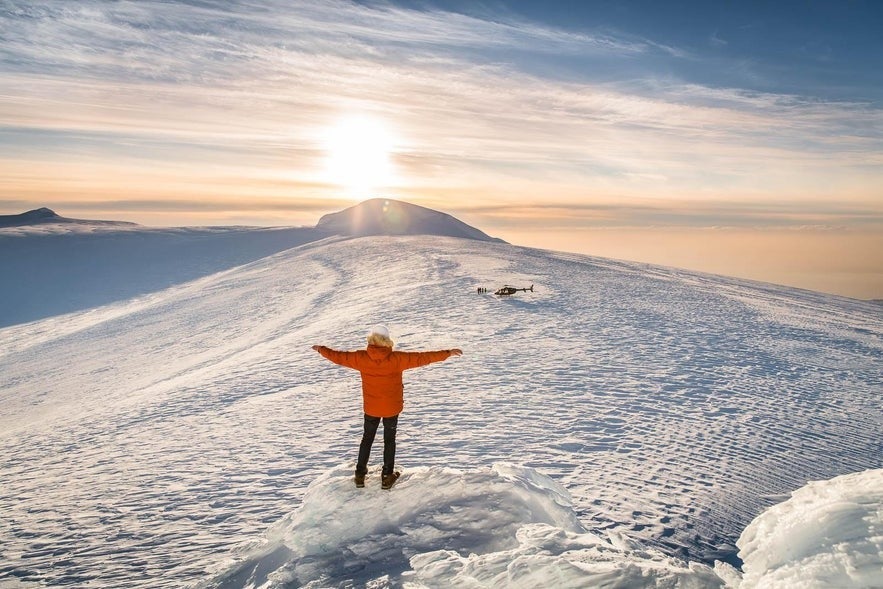 Person standing on the snowy summit of Langjokull Glacier in Iceland, watching the sunset over the icy landscape.