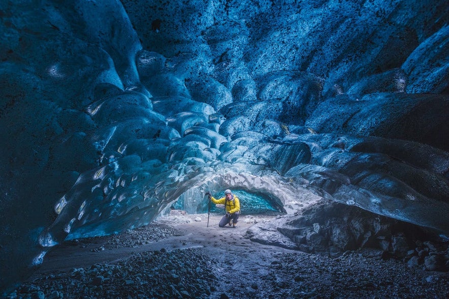 Traveler kneeling inside the blue ice tunnel of Katla Ice Cave beneath Myrdalsjokull Glacier in South Iceland.