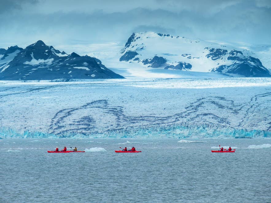 Viaggiatori che praticano kayaking sulla laguna glaciale Heinabergslon con vista sul ghiacciaio Heinabergsjokull e le cime innevate nel Parco Nazionale Vatnajokull.