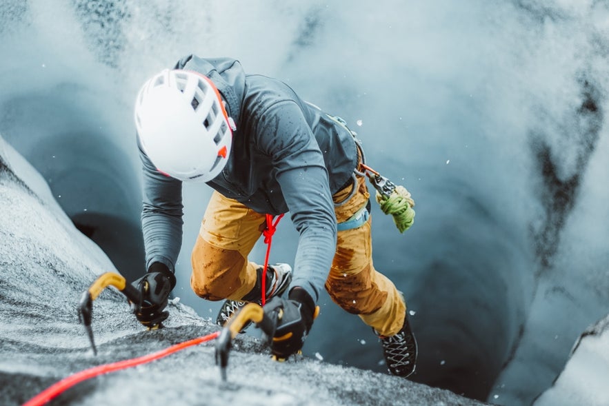 Ice climber using ice axes and ropes while ascending a crevasse on Solheimajokull Glacier in South Iceland.