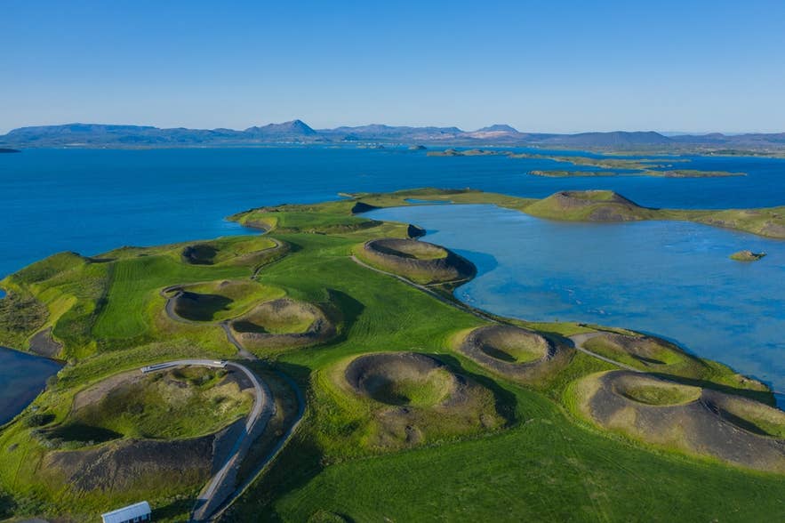 Aerial view of Lake Myvatn, Iceland, surrounded by green fields, water, and distant mountains under clear skies.