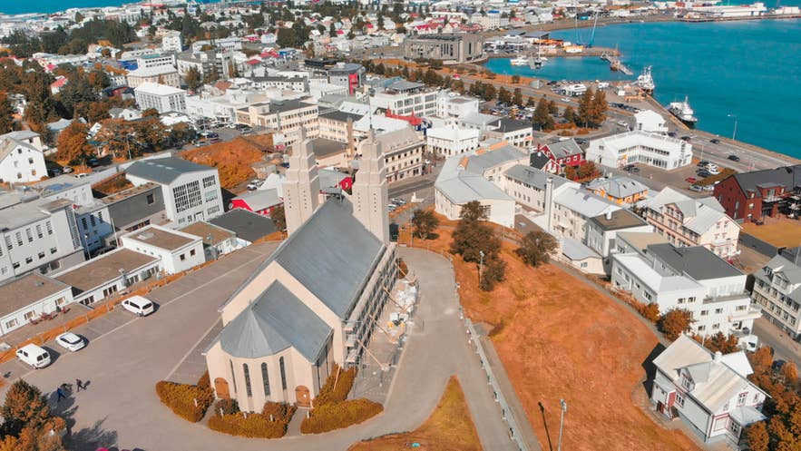 Vista aérea de Akureyri, Islandia, con iglesia de dos torres, puerto, barcos y vegetación bajo un cielo despejado.