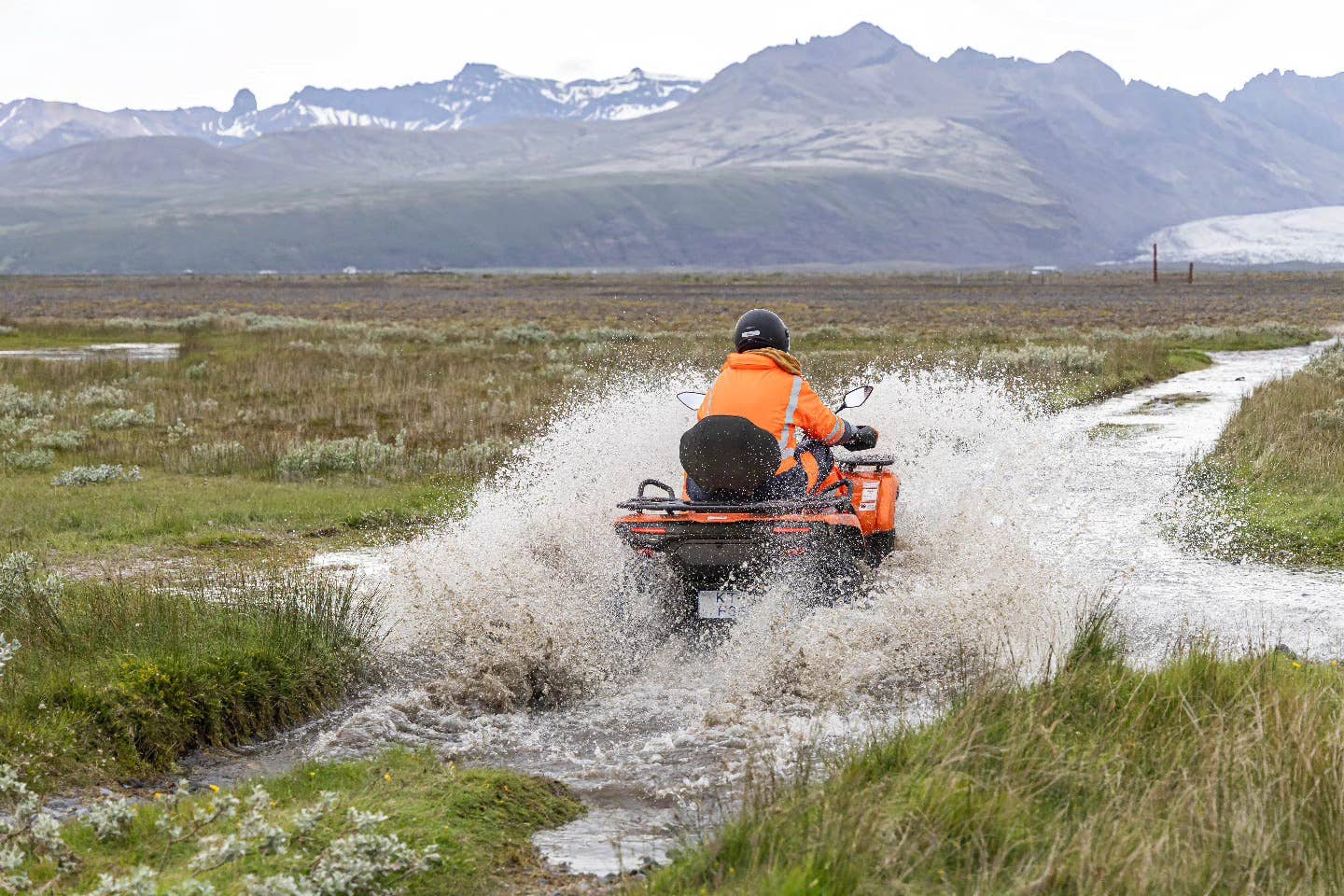 ATV rider in Iceland splashing through a shallow stream with glacier views nearby.
