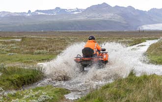 ATV rider in Iceland splashing through a shallow stream with glacier views nearby.