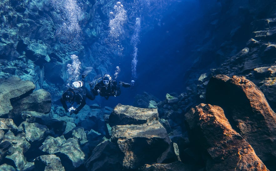 Scuba divers exploring the clear waters of Silfra Fissure in Thingvellir National Park, Iceland. Scuba divers exploring the clear waters of Silfra Fissure in Thingvellir National Park, Iceland.