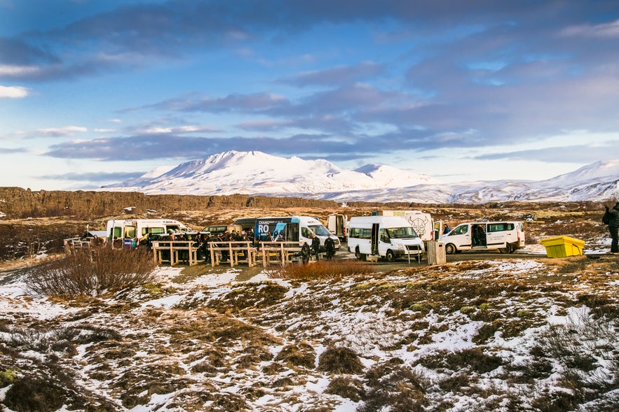 ลานจอดรถซิลฟราและจุดนัดพบในอุทยานแห่งชาติธิงเวลลิร์ ไอซ์แลนด์ มีรถตู้ทัวร์และวิวภูเขาหิมะ