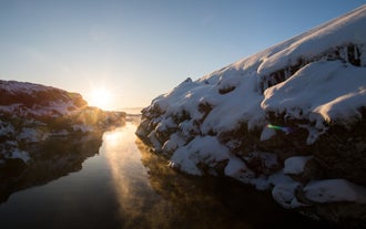 Silfra Fissure in winter features crystal-clear water and icy terrain, with the rift between continents glowing under a warm sunset.