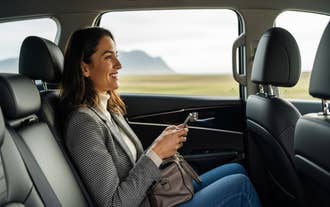 Passenger relaxing in a comfortable car seat, smiling while using her phone during a private transfer in Iceland.